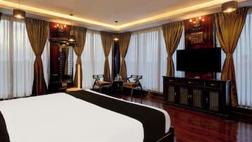 Een hotelkamer met een groot bed, twee stoelen, een televisie en gordijnen.