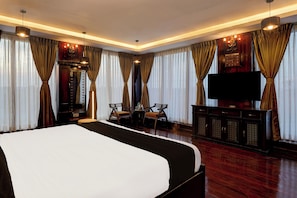 A hotel room with a large bed, two chairs, a TV, and curtains. - Townhouse NK Vivanta Luxury Rooms (Sriperumbudur)