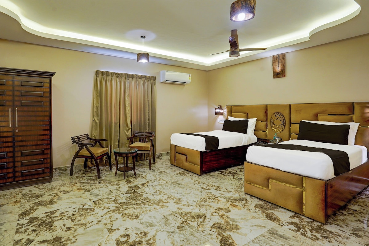 A hotel room with two beds, a desk, chairs, an air conditioning unit, and a ceiling fan.