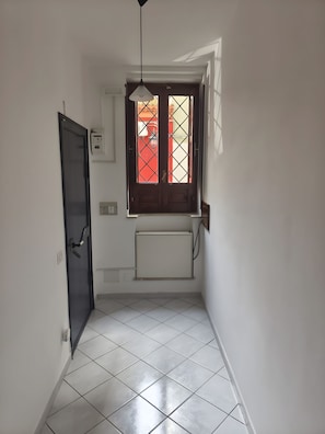 A narrow hallway with a tiled floor, a door, a window with a view, and a ceiling light fixture. - Apartment 'La Casa Di Sofi E Greta' with private garden, Wi-Fi and air conditioning (Augusta)