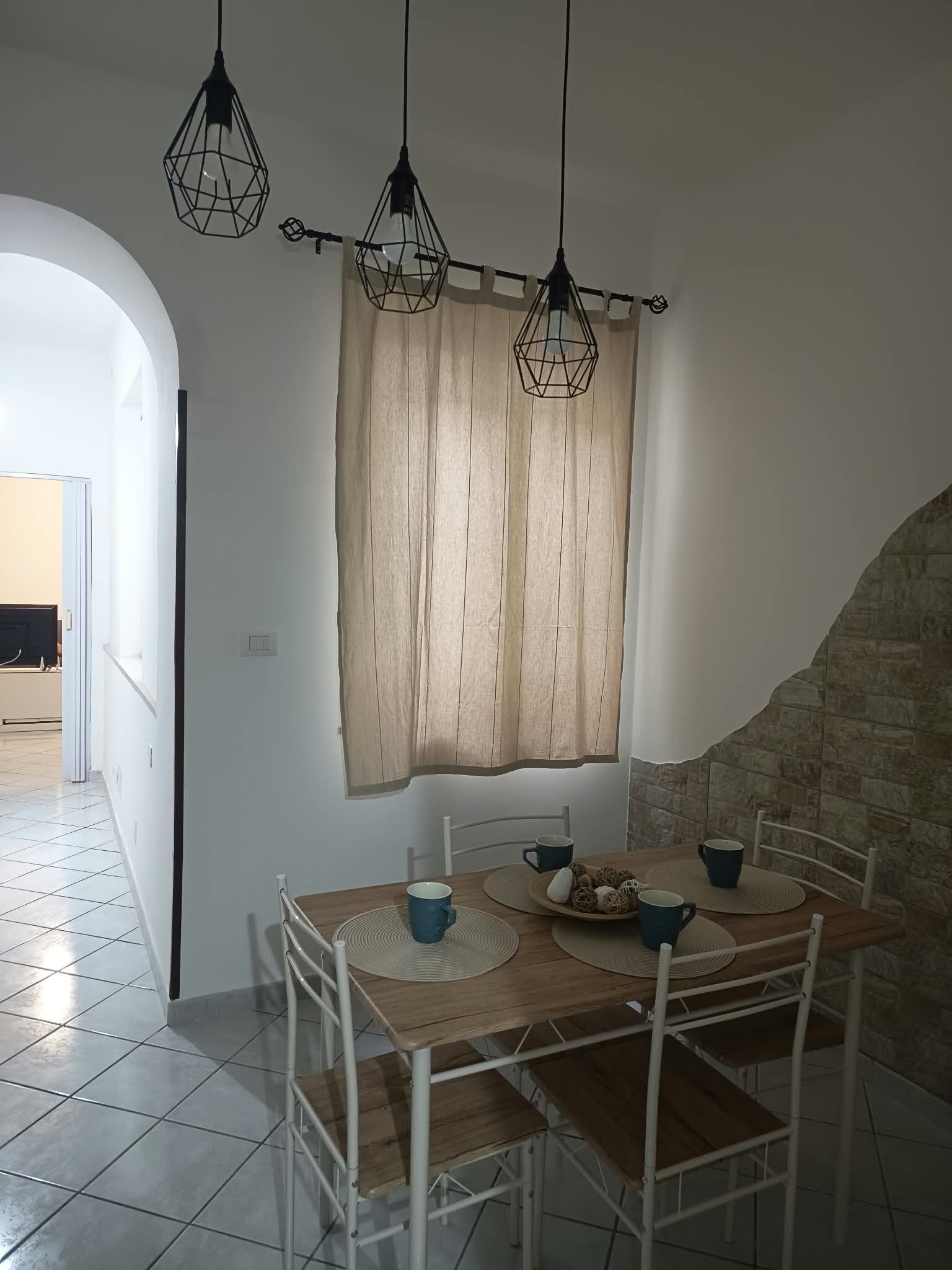 Un comedor con una mesa dispuesta para dos personas, una ventana con cortinas y una escalera que lleva a otra habitación.