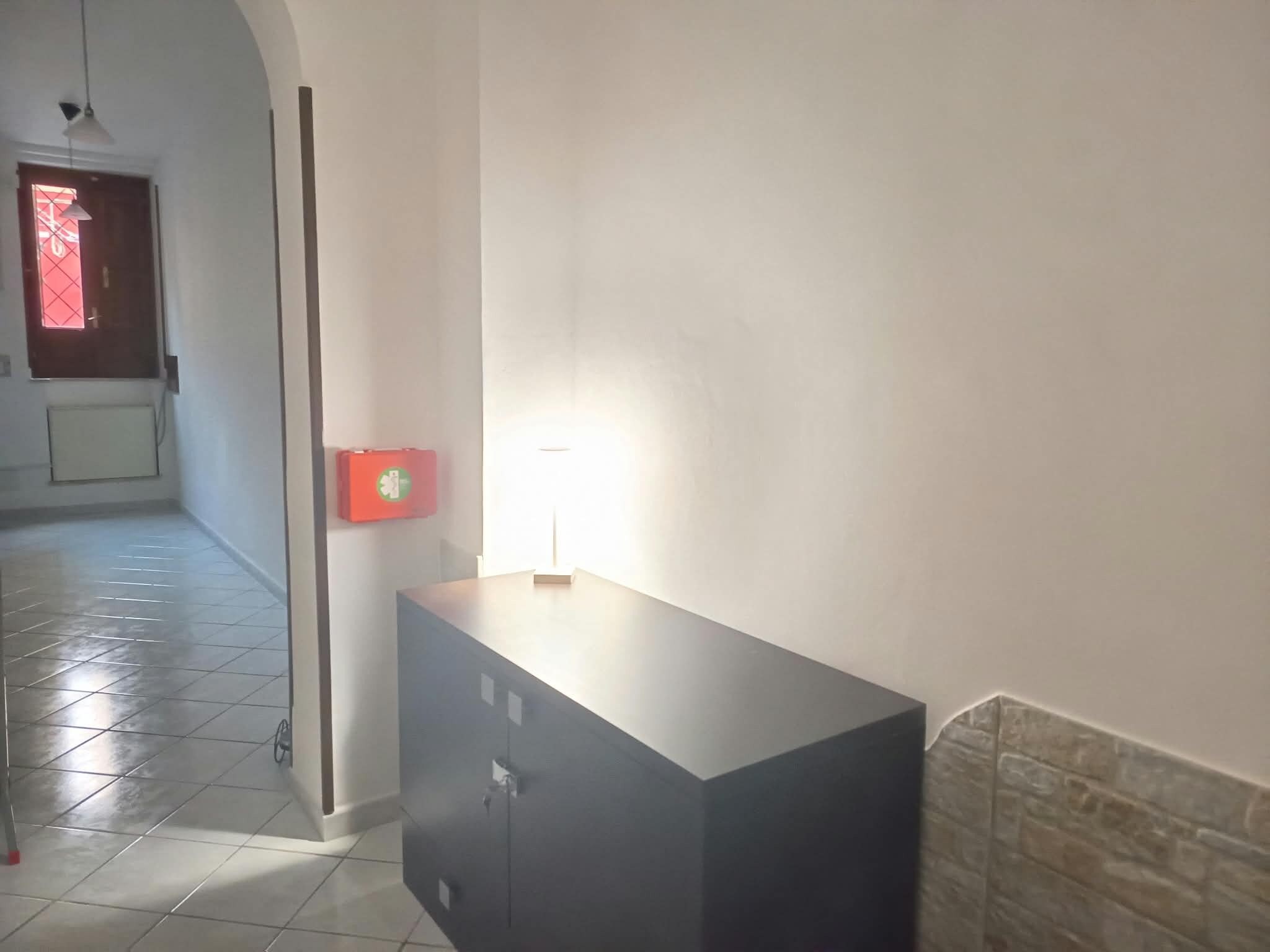 Ein Flur mit Fliesenboden, einer Tür mit rotem Fenster und einer Wandleuchte.
