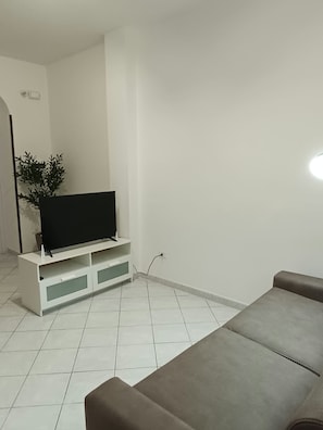 Ein Wohnzimmer mit einem Flachbildfernseher auf einem weißen Schrank, einem braunen Sofa und einer Zimmerpflanze.