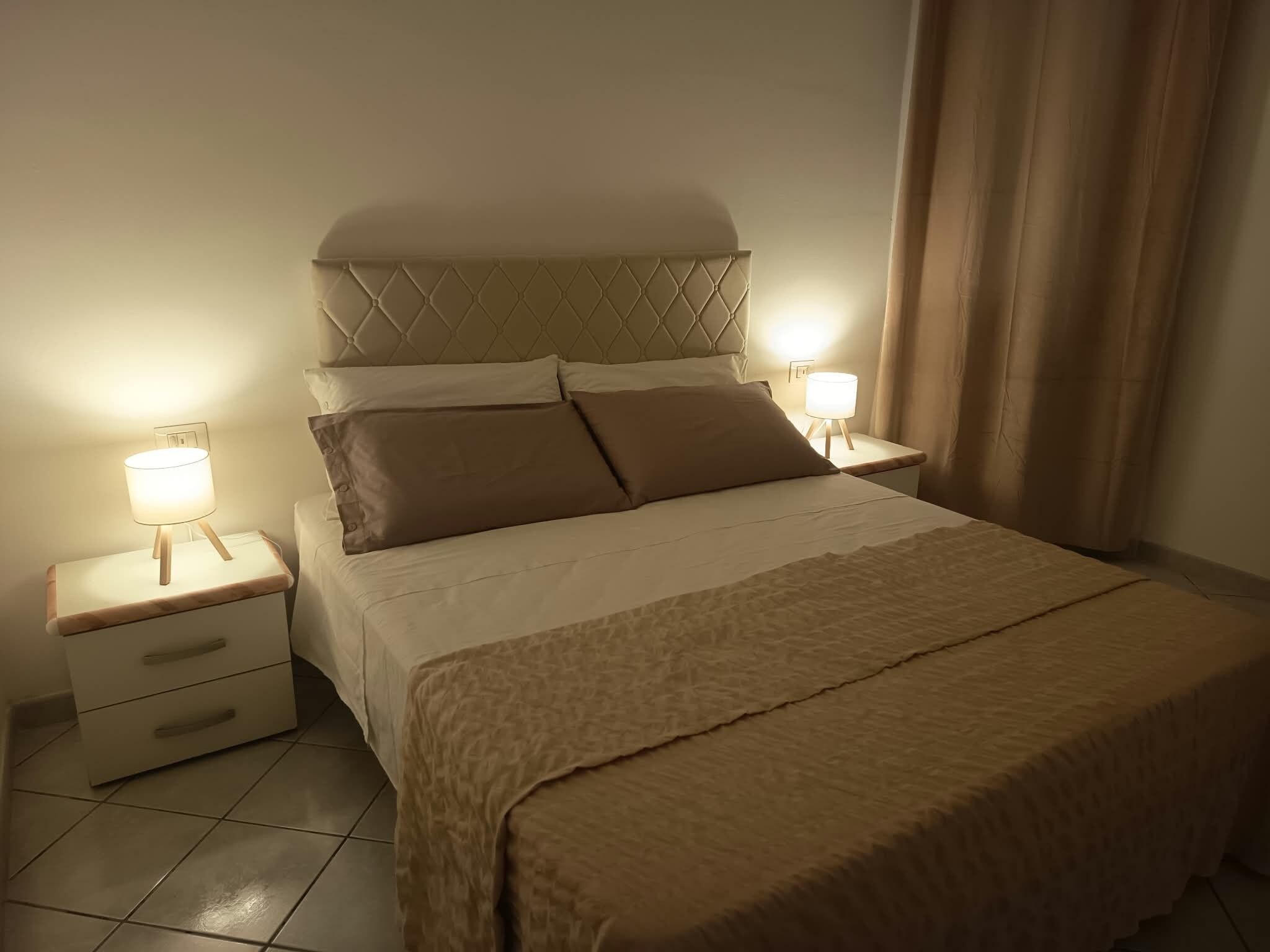Una cama bien hecha con cabecera, dos mesitas de noche con lámparas y una cómoda.