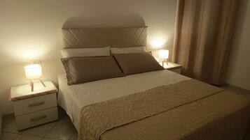 Una cama bien hecha con cabecera, dos mesitas de noche con lámparas y una cómoda.