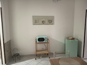 A small kitchenette with a teal-colored microwave on a wooden stand, a small table with a woven placemat, and a green cabinet with a basket on top. - Apartment 'La Casa Di Sofi E Greta' with private garden, Wi-Fi and air conditioning (Augusta)