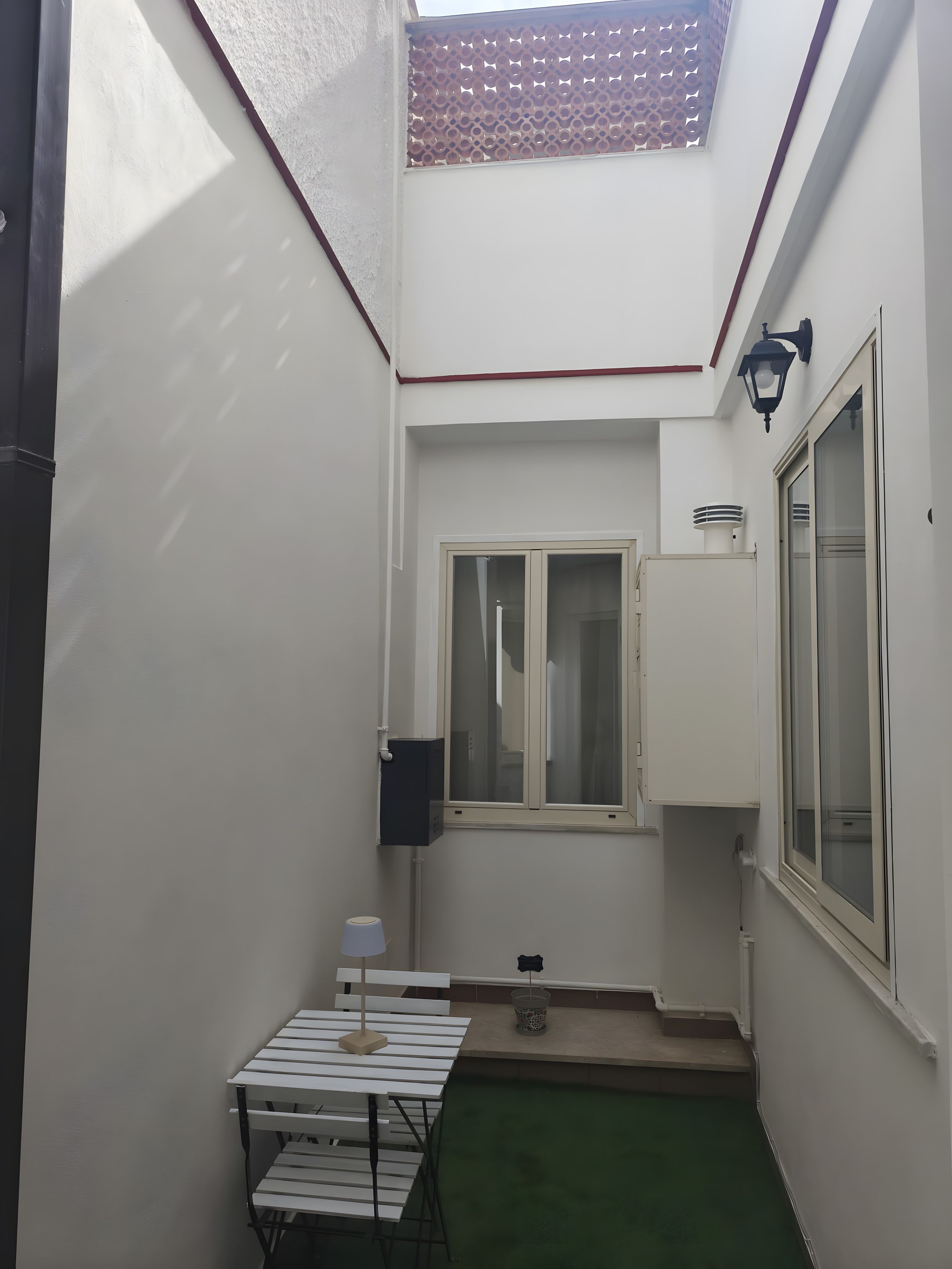 Un espacio exterior pequeño y cerrado con una mesa, una silla, una ventana y una puerta.
