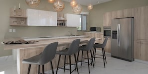 A modern kitchen with a central island, bar stools, a stainless steel refrigerator, and pendant lighting. - Sunrise Suites All Inclusive (Puerto Plata)