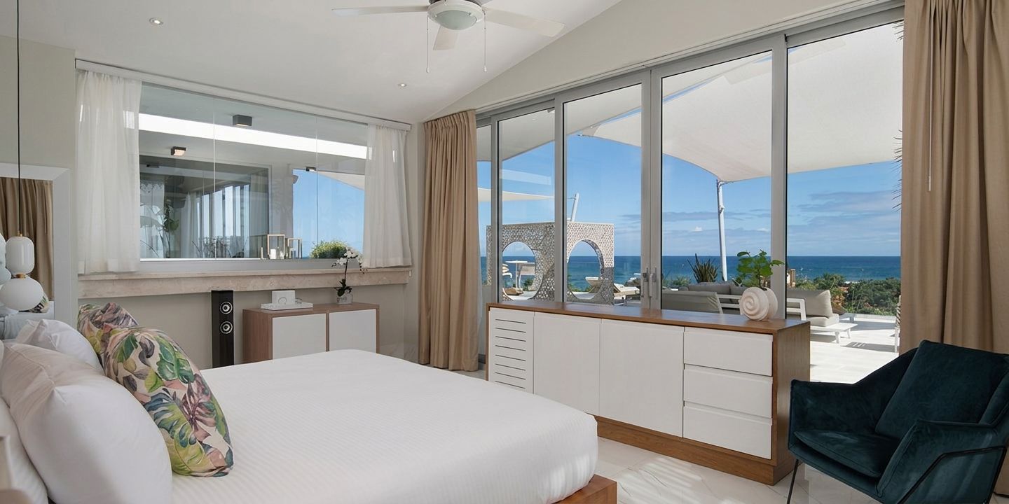 A modern hotel room with a large bed, a desk, and a view of the sea.