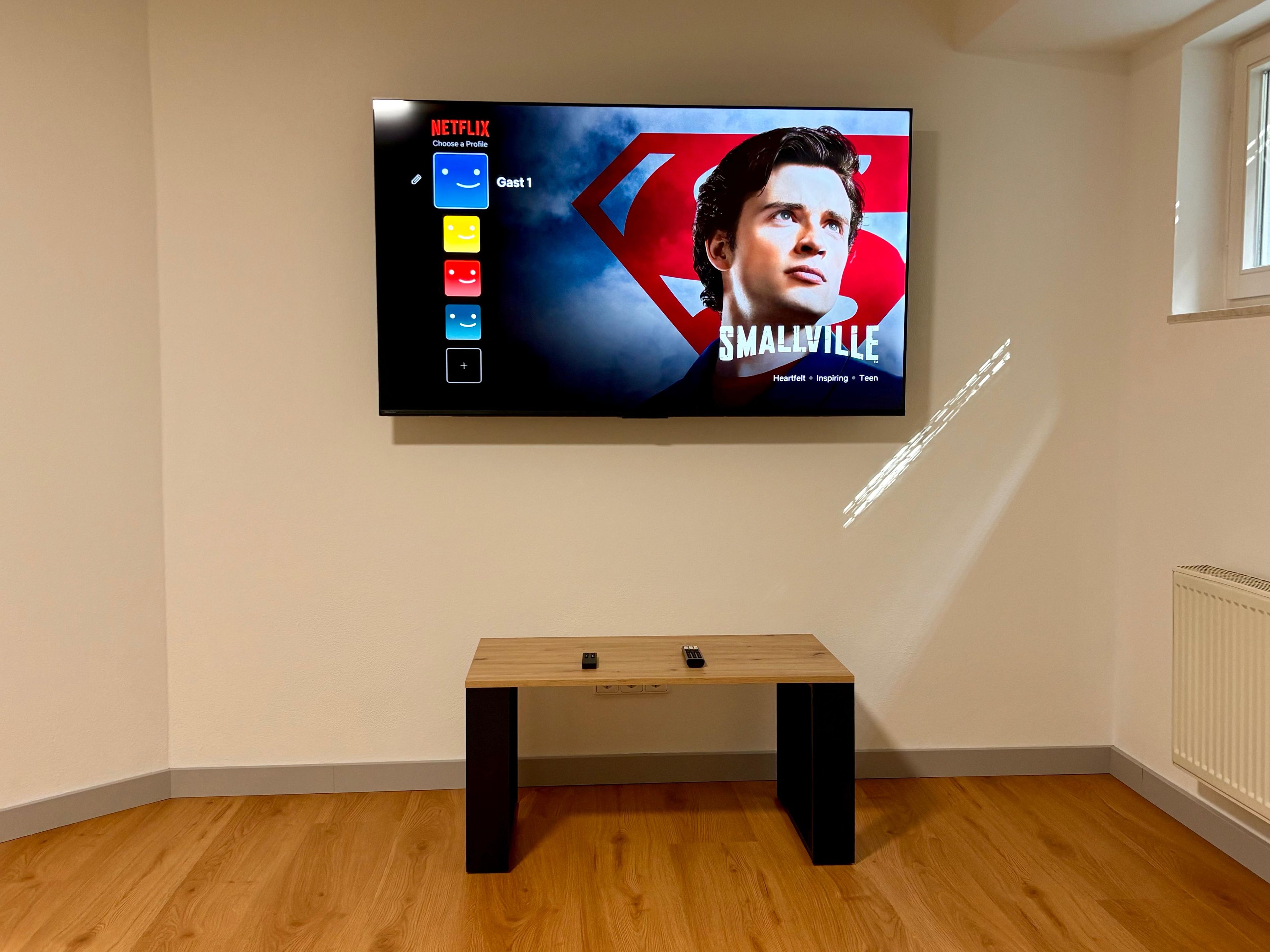 A television mounted on a wall displaying a movie poster for 'Smallville.'