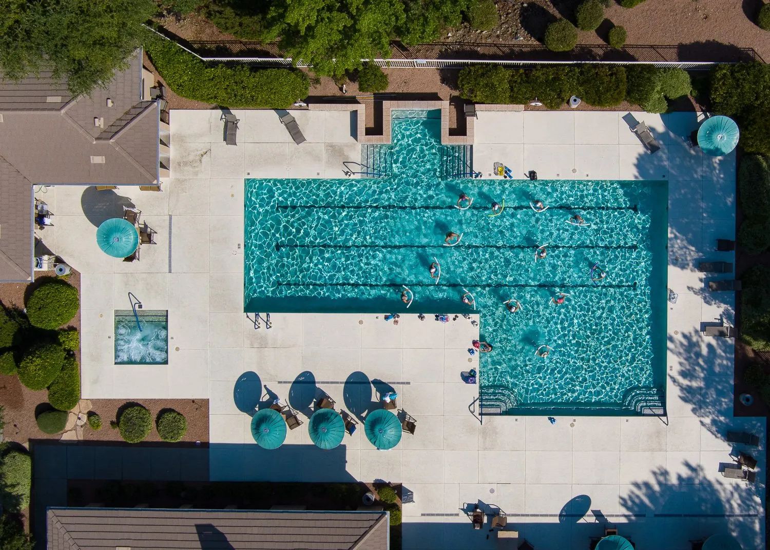 An aerial view of a swimming pool area with multiple lanes, lounge chairs, and umbrellas.