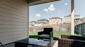 A covered patio with wicker furniture and a glass table, overlooking a residential neighborhood. -  Cozy Comfort Home near Randolph AFB, Fort Sam& I 10 -Spacious 5-bedroom house (Converse)