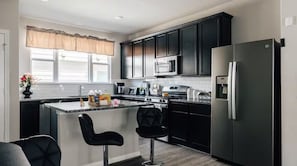 A modern kitchen with dark cabinets, a stainless steel refrigerator, and a central island with two bar stools. -  Cozy Comfort Home near Randolph AFB, Fort Sam& I 10 -Spacious 5-bedroom house (Converse)