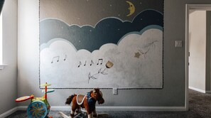 A child's room with a wall mural of clouds, stars, and a crescent moon. -  Cozy Comfort Home near Randolph AFB, Fort Sam& I 10 -Spacious 5-bedroom house (Converse)