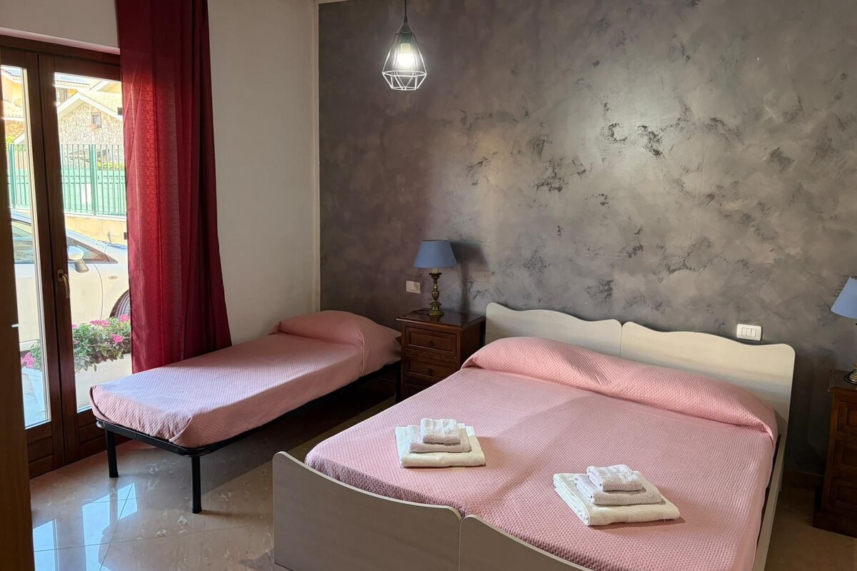 A bedroom with two beds, a red curtain, a lamp, and a textured wall.