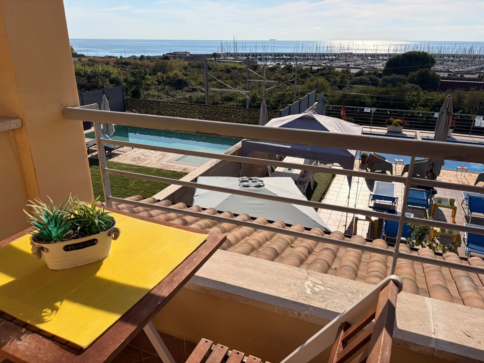 Un balcón con vistas a un puerto deportivo, una piscina y una costa lejana.