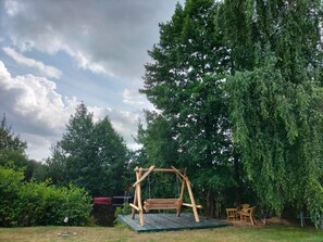 A wooden swing set in a backyard with a green mat, surrounded by trees and a cloudy sky. - NEW! Lakefront vacation home with sauna (Twist)