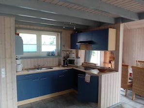 A compact kitchen with blue cabinets, a microwave, a coffee maker, and a window. - NEW! Lakefront vacation home with sauna (Twist)