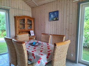 A dining area with a table set for four, surrounded by wicker chairs, a wooden cabinet with glass doors, and a painting on the wall. - NEW! Lakefront vacation home with sauna (Twist)