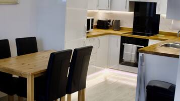 Een moderne keuken met witte kasten, een houten eettafel en zwarte stoelen.