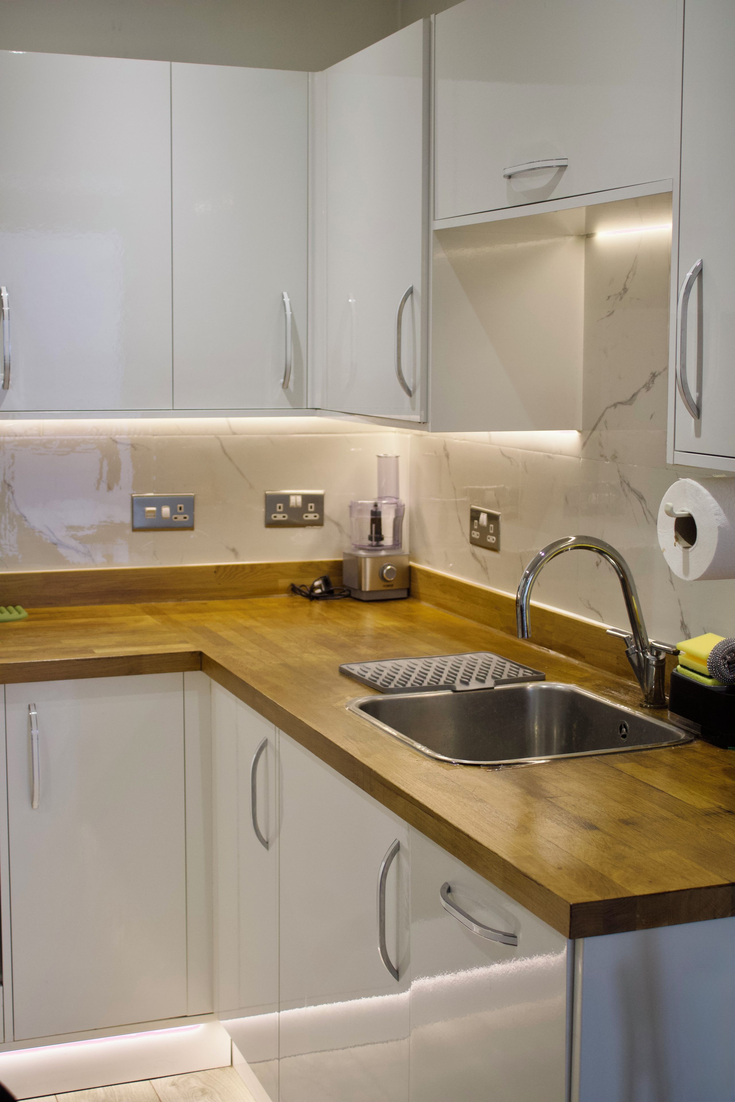 Een moderne keuken met witte kastjes, een houten aanrechtblad, een RVS-gootsteen en een inbouwoven.