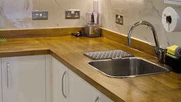Een moderne keuken met witte kastjes, een houten aanrechtblad, een RVS-gootsteen en een inbouwoven.