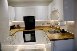 A modern kitchen with white cabinets, a black oven, a wooden countertop, and a stainless steel sink. - Ivory Nest (Harlow)