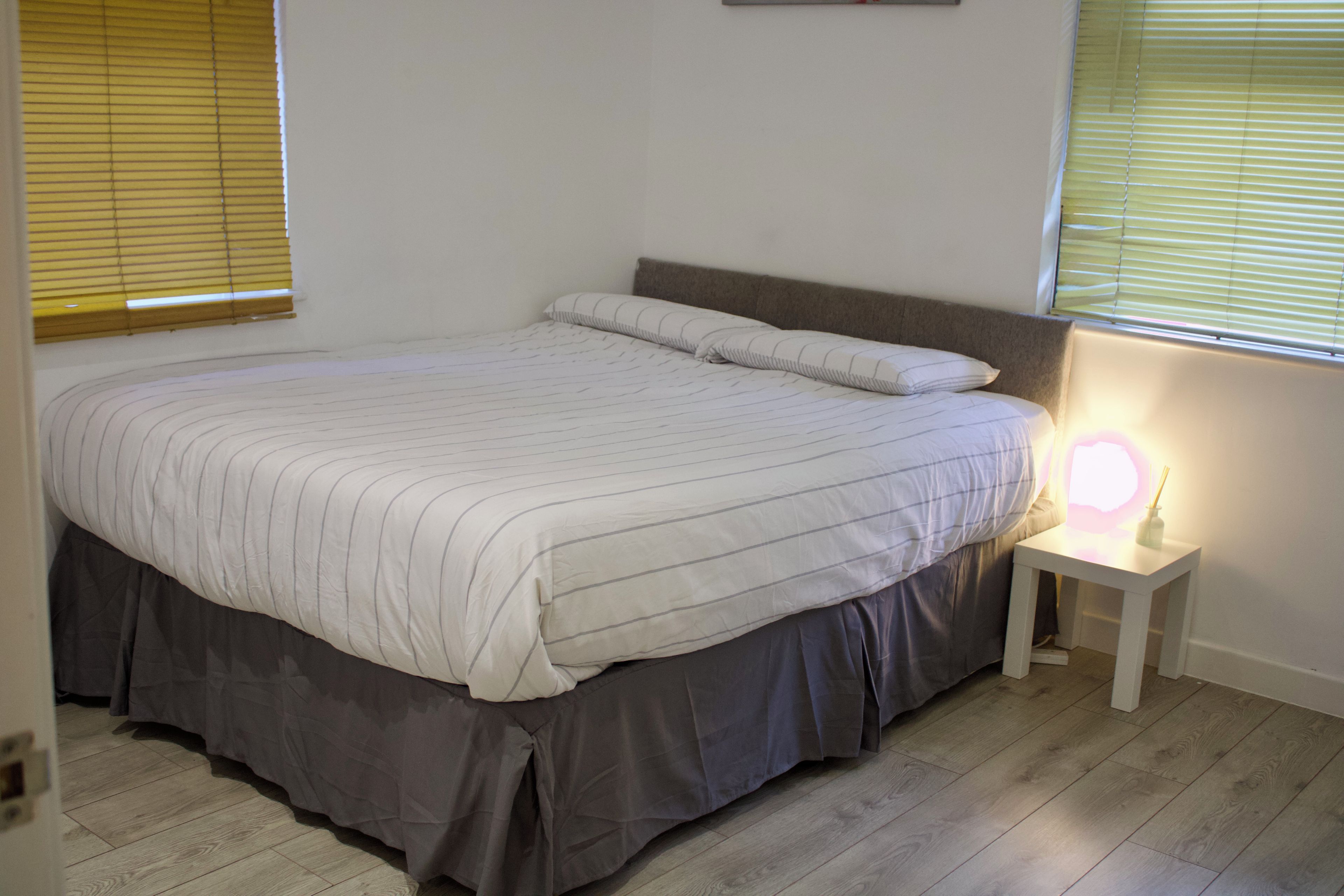 Een slaapkamer met een bed, nachtkastje en een raam met zonwering.
