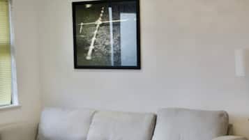 Een woonkamer met een hoekbank, een salontafel, een vloerkleed en een ingelijst kunstwerk aan de muur.
