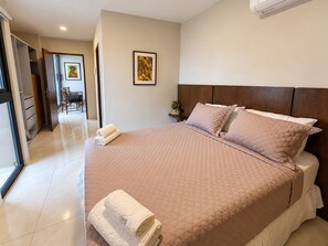 Habitación de hotel con una cama grande, una mesita de noche con una planta y vistas al pasillo.