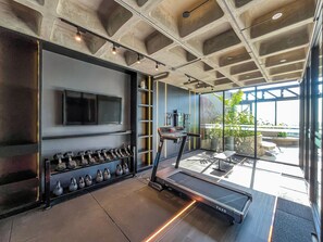 Un gimnasio moderno con una cinta de correr, pesas y un televisor en la pared.
