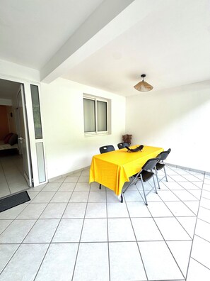 A dining area with a yellow tablecloth, four chairs, a window, and a ceiling fan.