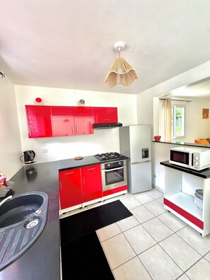 A compact kitchen with red cabinets, a black countertop, a gas stove, a microwave, and a refrigerator.