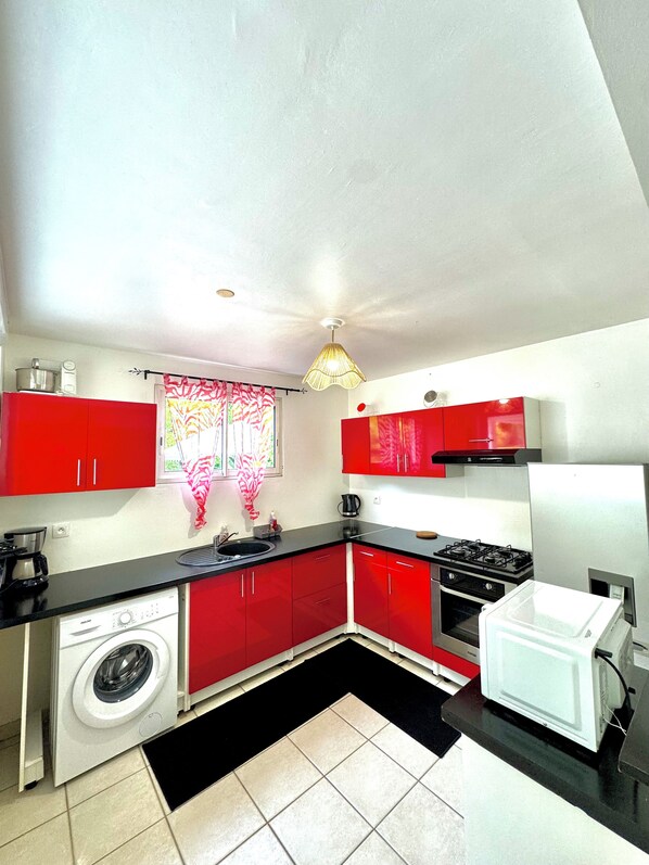 A compact kitchen with red cabinets, a washing machine, a microwave, and a gas stove.