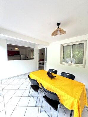 A dining area with a yellow table, black chairs, a woven ceiling light, and a window with a view.