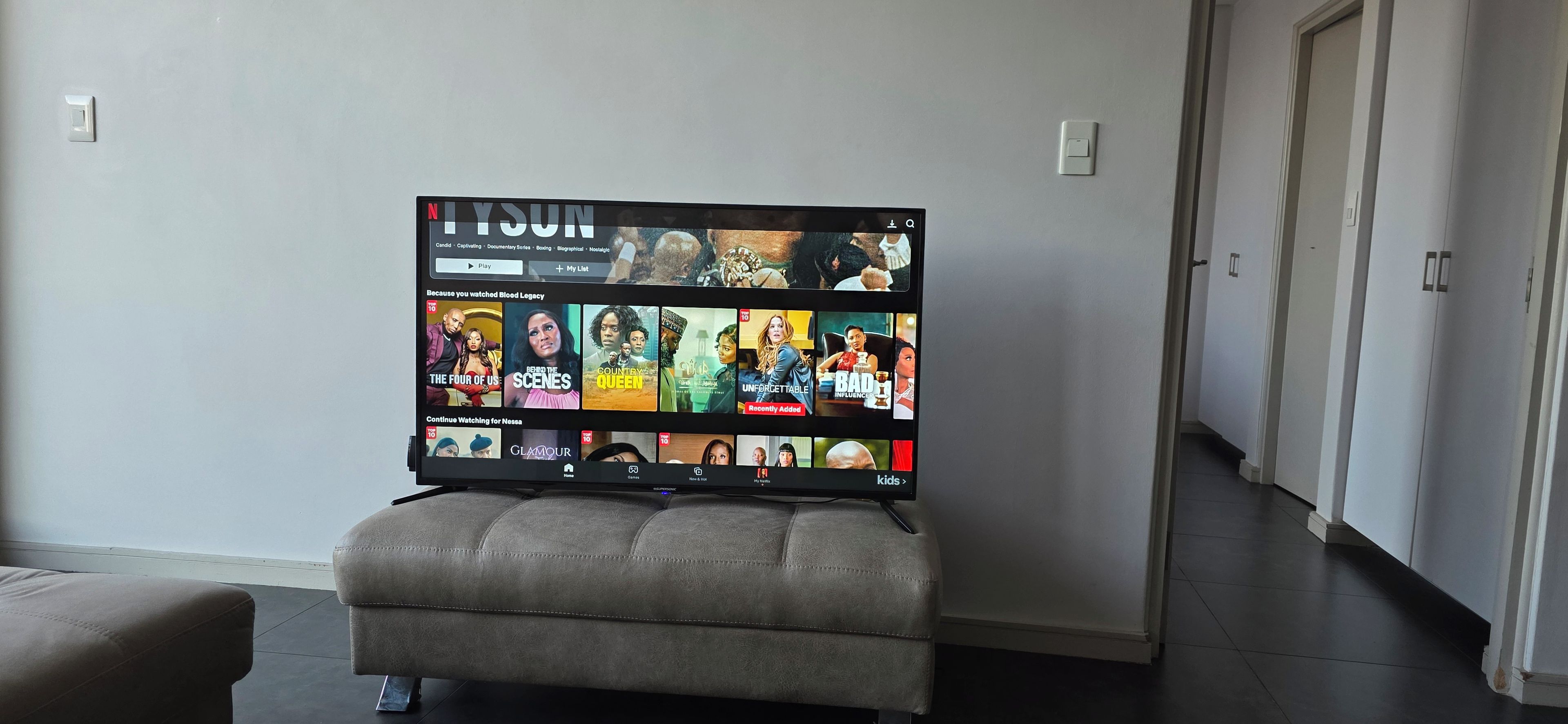 A flat-screen TV mounted on a wall with a selection of streaming content displayed.