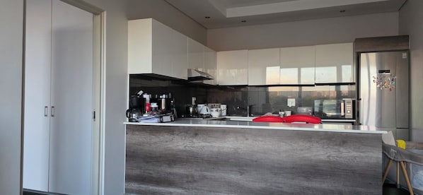 A modern kitchen with white cabinets, a stainless steel refrigerator, and a red chair. - Room-cozy Apartment Rental in Germiston (Germiston)