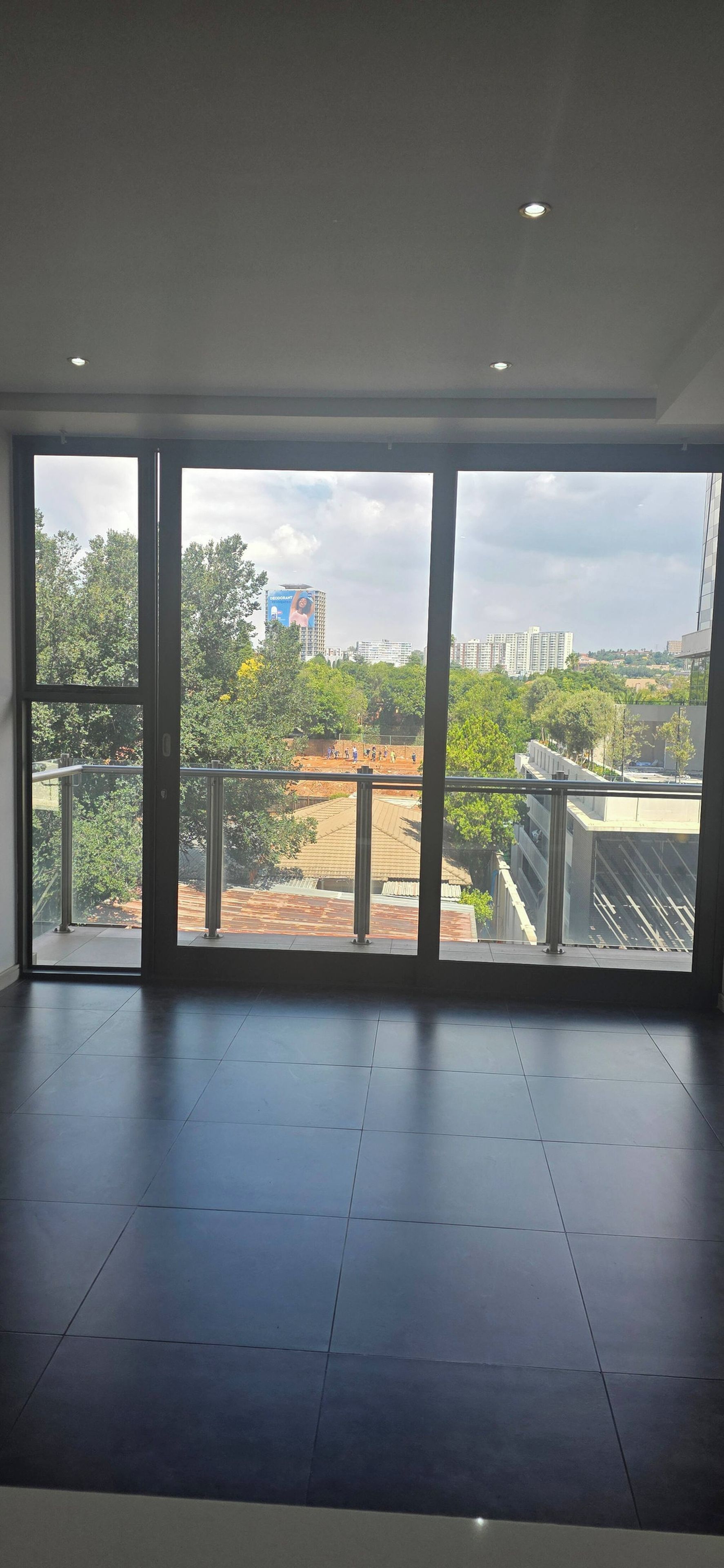 Una habitación con ventanas amplias, suelo de baldosas y vista a un paisaje urbano con edificios y árboles.
