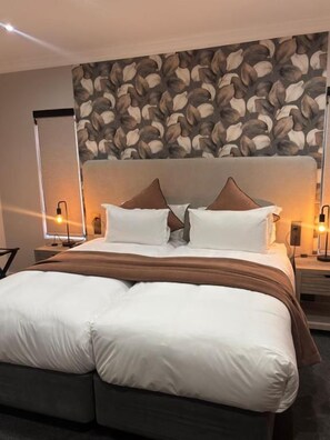 Una habitación de hotel con una cama grande, dos lámparas de noche y un papel tapiz estampado.