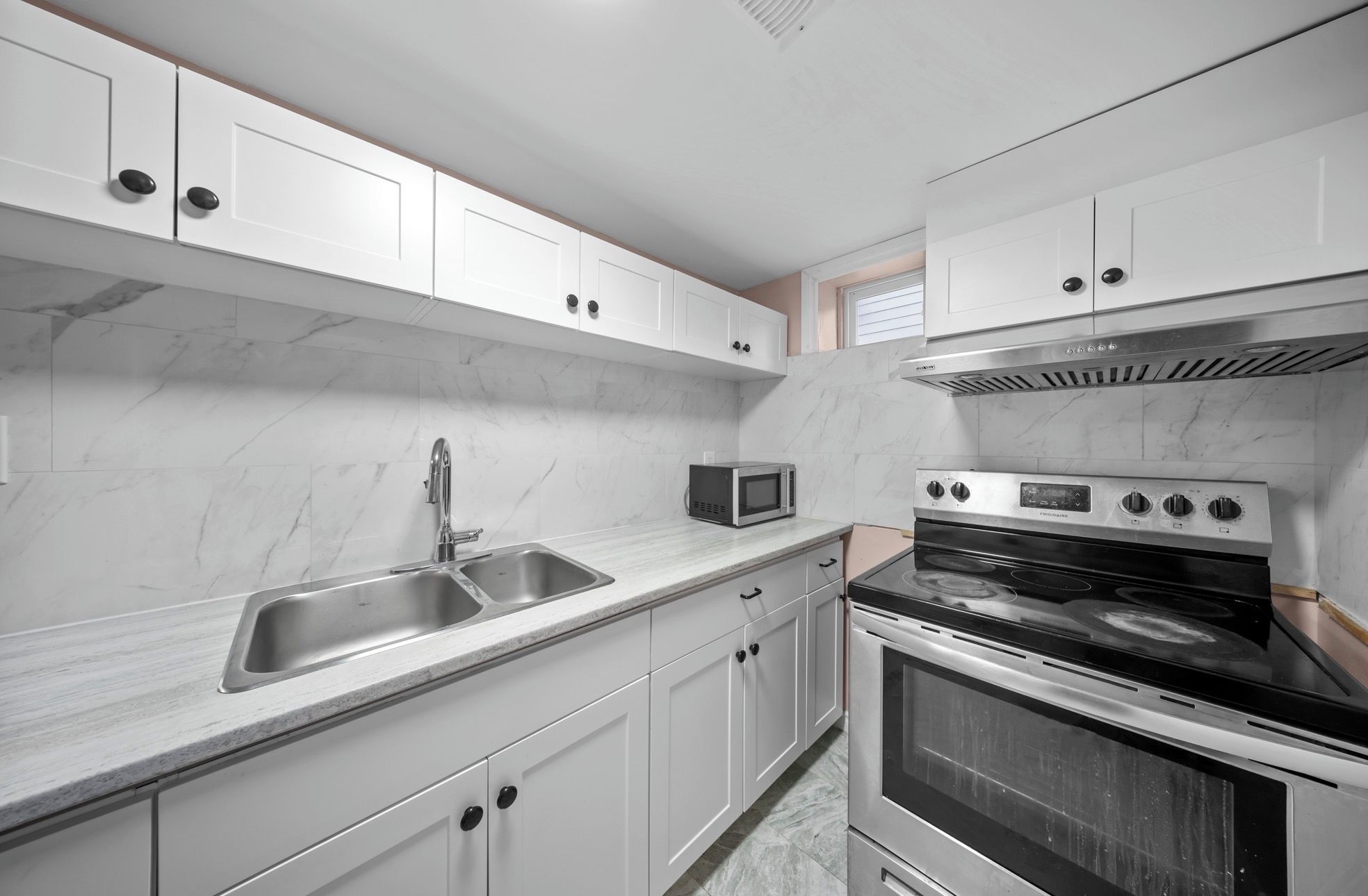 Een moderne keuken met witte kastjes, een roestvrijstalen spoelbak, een magnetron en een inbouwoven.
