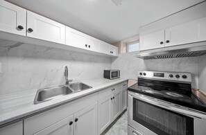Een moderne keuken met witte kastjes, een roestvrijstalen spoelbak, een magnetron en een inbouwoven.