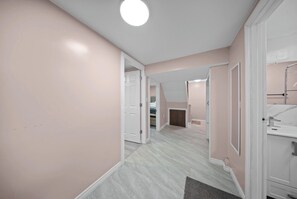 Een gang met een deur naar een slaapkamer, een badkamer met een spiegel, en een plafondlamp.