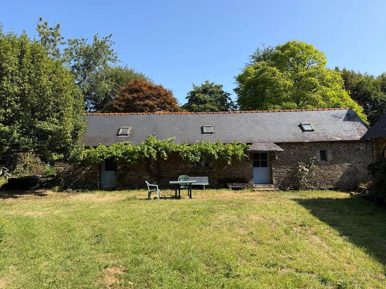 A stone building with a sloped roof, a small porch, and a bench in the yard.