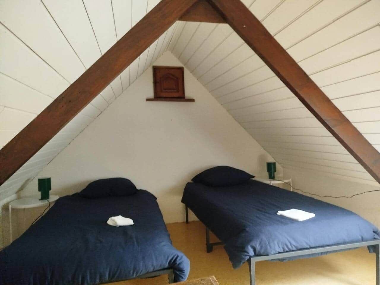 A room with two single beds, a wooden ceiling, and a small picture frame on the wall.