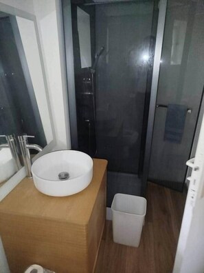 A bathroom with a white sink, a mirror, a shower, and a trash bin. - Welcoming 2-bedroom house in charming Motreff for your getaway (Motreff)