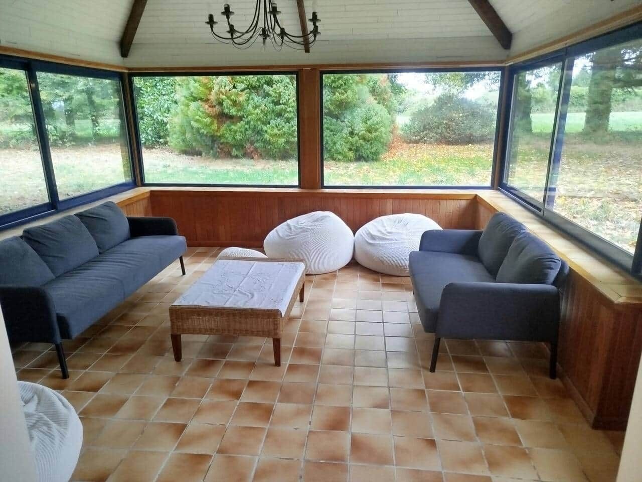 Un salón de estar con ventanal amplio, sofá oscuro, un pouf blanco y mesa de centro de madera.