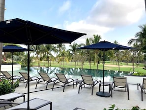 Zona junto a la piscina con sillas de descanso y sombrillas, con vista a un campo de golf.