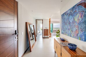 A modern hallway with a wooden door, a large mirror, and a wooden cabinet with a bowl. - Luxury 2BR Condo - Marina & Golf Views, Resort Pool, Gym & Jacuzzi (Puerto Vallarta)
