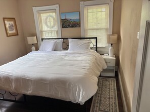 A neatly made bed with white linens, a bedside table with a lamp, and a framed picture on the wall. - Cozy Home in SE Washington, DC (Washington)