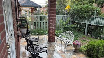 A covered patio with two white metal chairs and a black metal table.